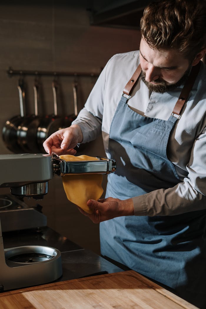 Male chef in kitchen making fresh pasta using a pasta machine.